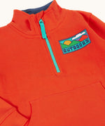 A close up of the front of the Frugi Half Zip Organic Cotton Papaya orange Jumper with large Outdoors colour block style graphic.