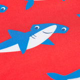 A close up of on of the sharks on the happy hammerheads print on the Frugi sun safe swimwear set. Blue and white hammerhead shark with a smiley face on a red coloured background.