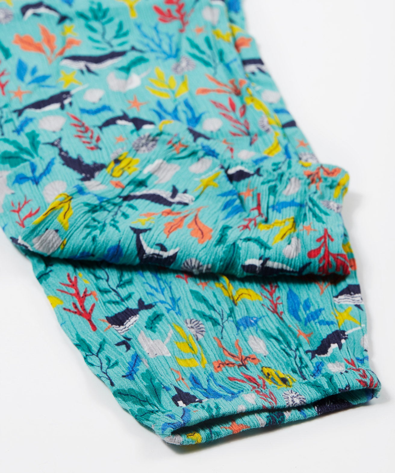 A close up of Frugi Eira Harems folded legs, featuring a Sea Life print which includes different sea animals and colourful seaweed and coral on a mint blue background.
