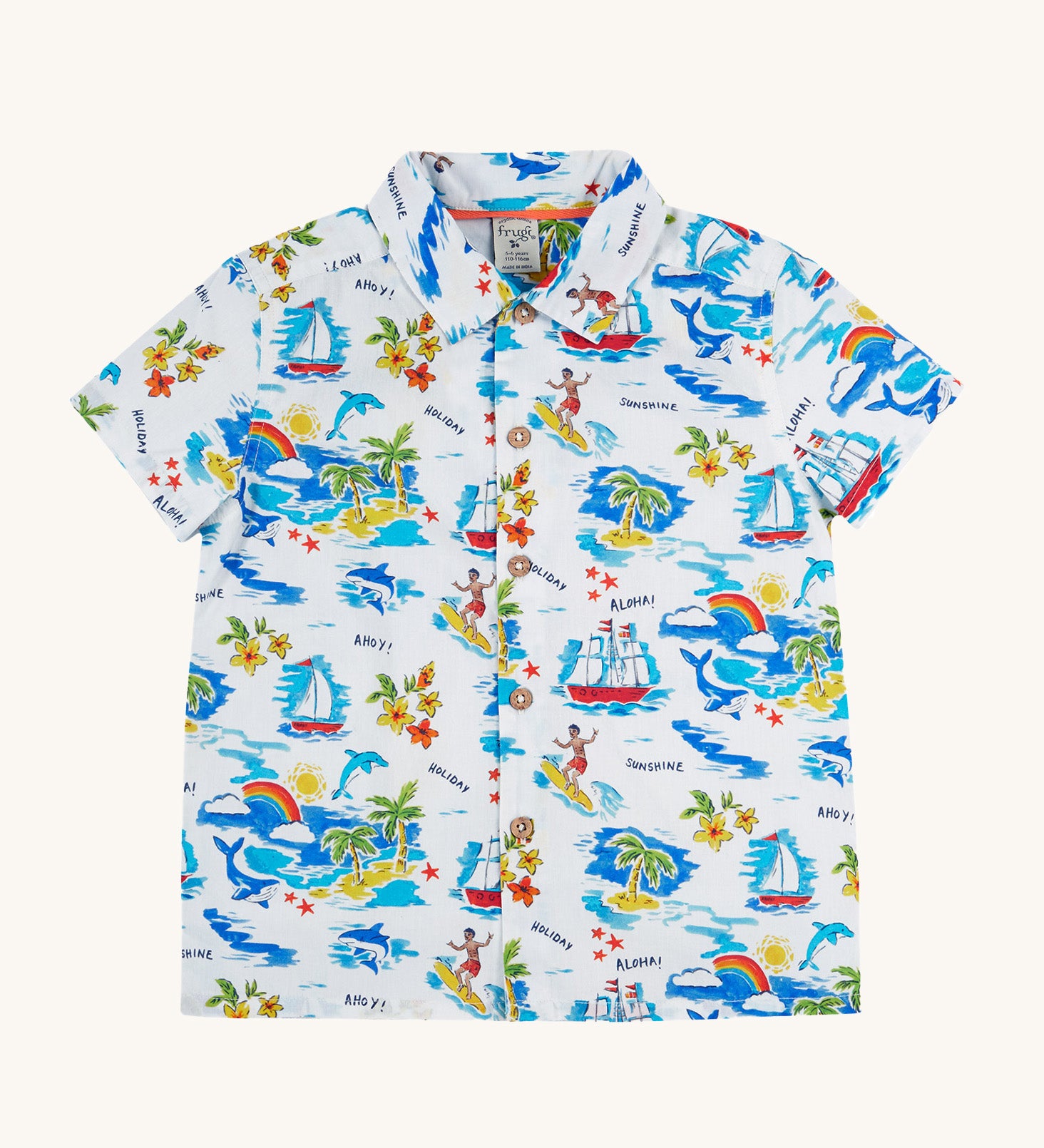 Frugi Harvey Hawaiian Shirt in a Aloha print, laid flat. Featuring a all-over tropical print with sailing ships, dolphins, rainbows, palm trees, surfers, and beach motifs on a white background, with wooden buttons down the middle.