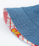 Close up of the Frugi kids hattie reversible hat - showing the denim detail and the white square with red lines and flower design on the flip side of the bucket hat on a organic cotton fabric