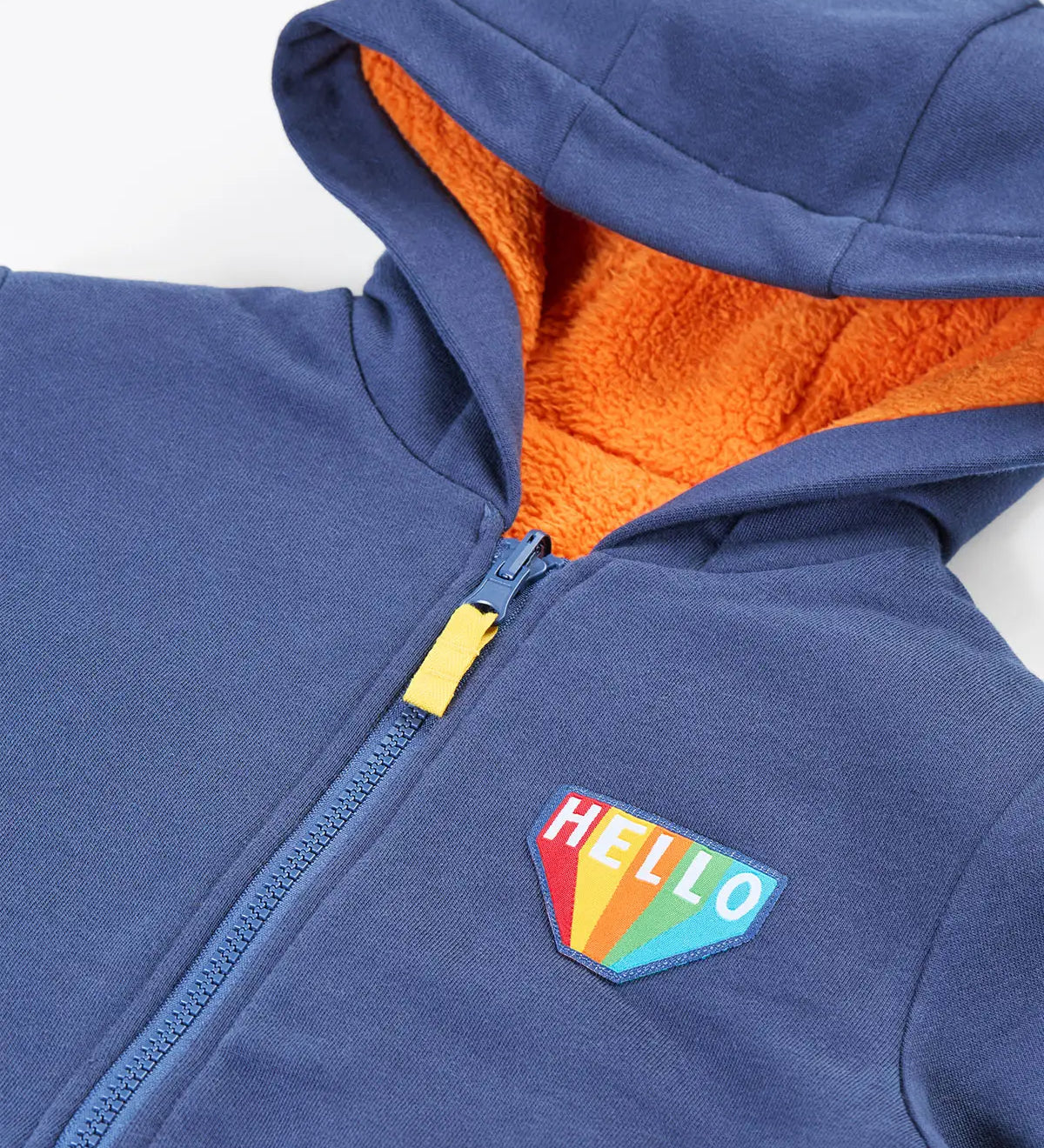 Close up of the hello badge on the front of the Frugi Helston reversible hoodie jacket. One side is navy cotton with a hello badge design on the chest  with a orange fleece body and yellow sleeves on the other. 