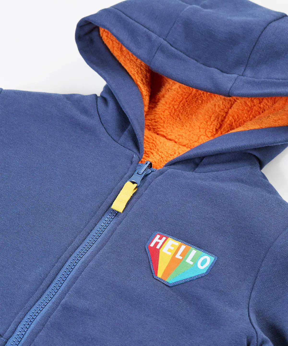 Close up of the hello badge on the front of the Frugi Helston reversible hoodie jacket. One side is navy cotton with a hello badge design on the chest  with a orange fleece body and yellow sleeves on the other. 