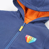 Close up of the hello badge on the front of the Frugi Helston reversible hoodie jacket. One side is navy cotton with a hello badge design on the chest  with a orange fleece body and yellow sleeves on the other. 