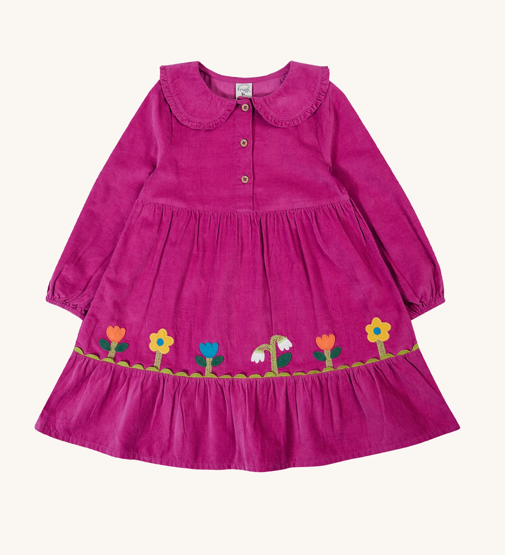 Frugi kids holly dress in damson flowers available at Babipur. A 100% GOTS organic cotton corduroy dress in bright purple with flower appliques on the skirt. Features a frilled collar and button fasteners. 