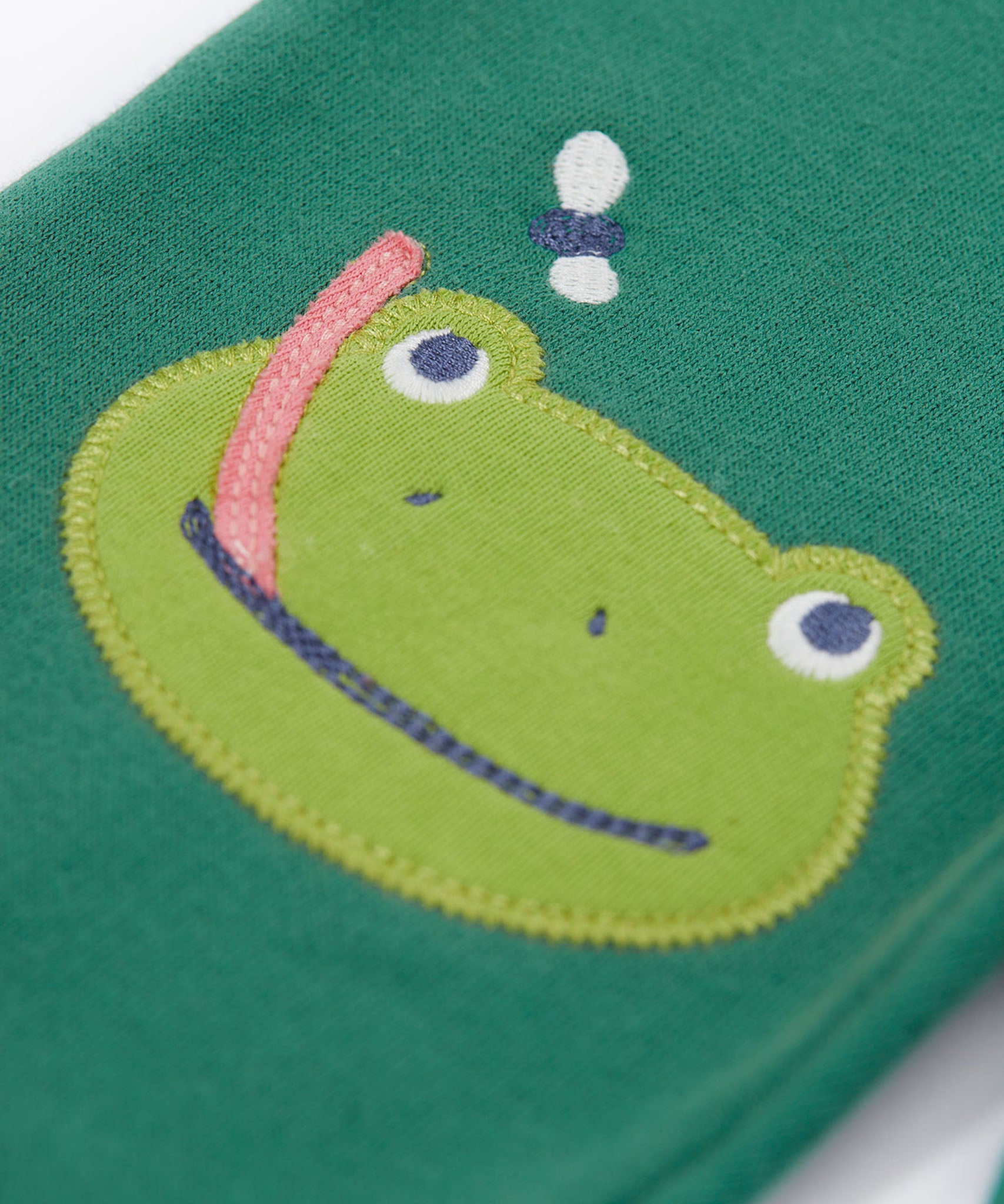 A close up of the frog applique on the knee on the Frugi holly green coloured frog beaver crawlers kids organic ccotton joggers. 