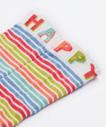 A close up of the Frugi kids hygge knee high sock. Showing the happy slogan on the white leg cuff on multicoloured striped organic cotton fabric