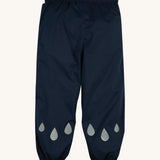 The front of the Frugi Indigo Navy coloured Rain Or Shine waterproof Trousers. The trousers have rain drop shaped reflective patches on the lower leg.