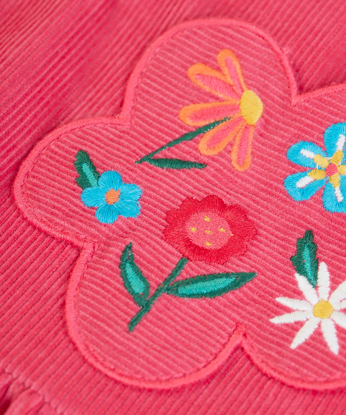Close up of the flowers embroidery on the front of the Frugi Isla pink rose dungaree dress with.