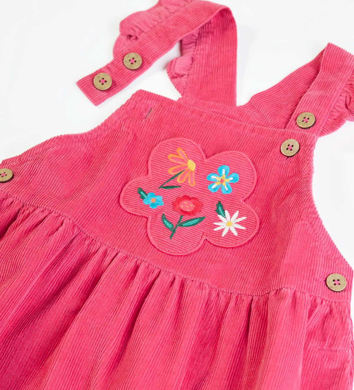 Close up of the front showing the frilled edge straps of the Frugi Isla pink rose dungaree dress with flowers embroidery on the front.