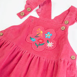 Close up of the front showing the frilled edge straps of the Frugi Isla pink rose dungaree dress with flowers embroidery on the front.