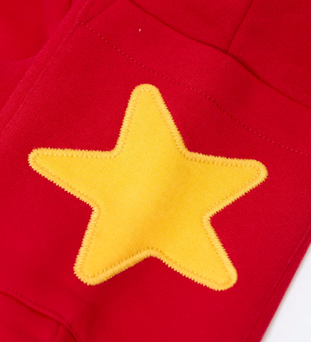 Close up of the yellow star applique on the side pocket of the Frugi journey joggers in scarlet red .