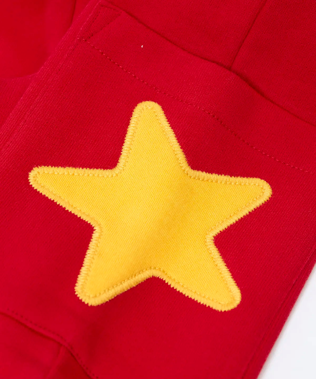 Close up of the yellow star applique on the side pocket of the Frugi journey joggers in scarlet red .