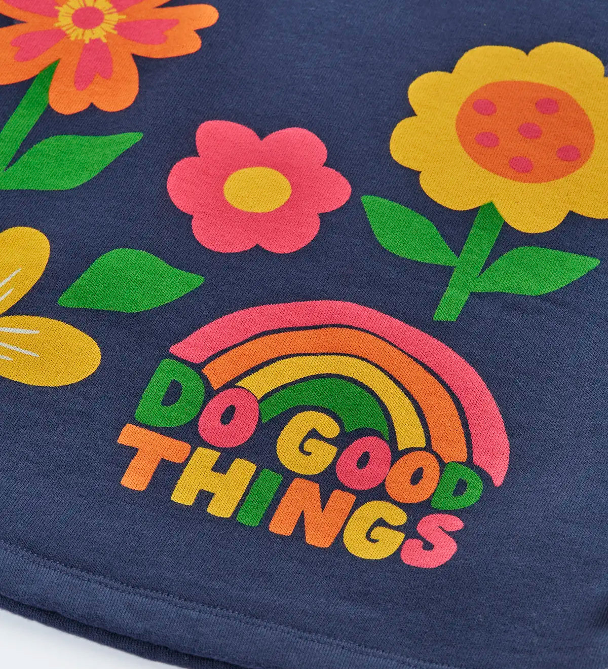 Close up of the rainbow do good things slogan design on the front of the Frugi Kari long sleeved dress in navy.