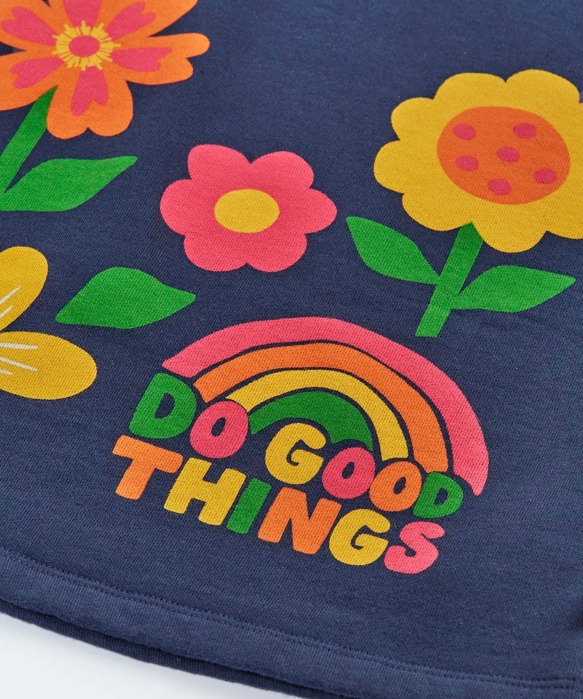 Close up of the rainbow do good things slogan design on the front of the Frugi Kari long sleeved dress in navy.