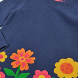 Close up of the Frugi Kari long sleeved dress in navy with flowers and do good things rainbow slogans along the hemline.