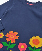 Close up of the Frugi Kari long sleeved dress in navy with flowers and do good things rainbow slogans along the hemline.