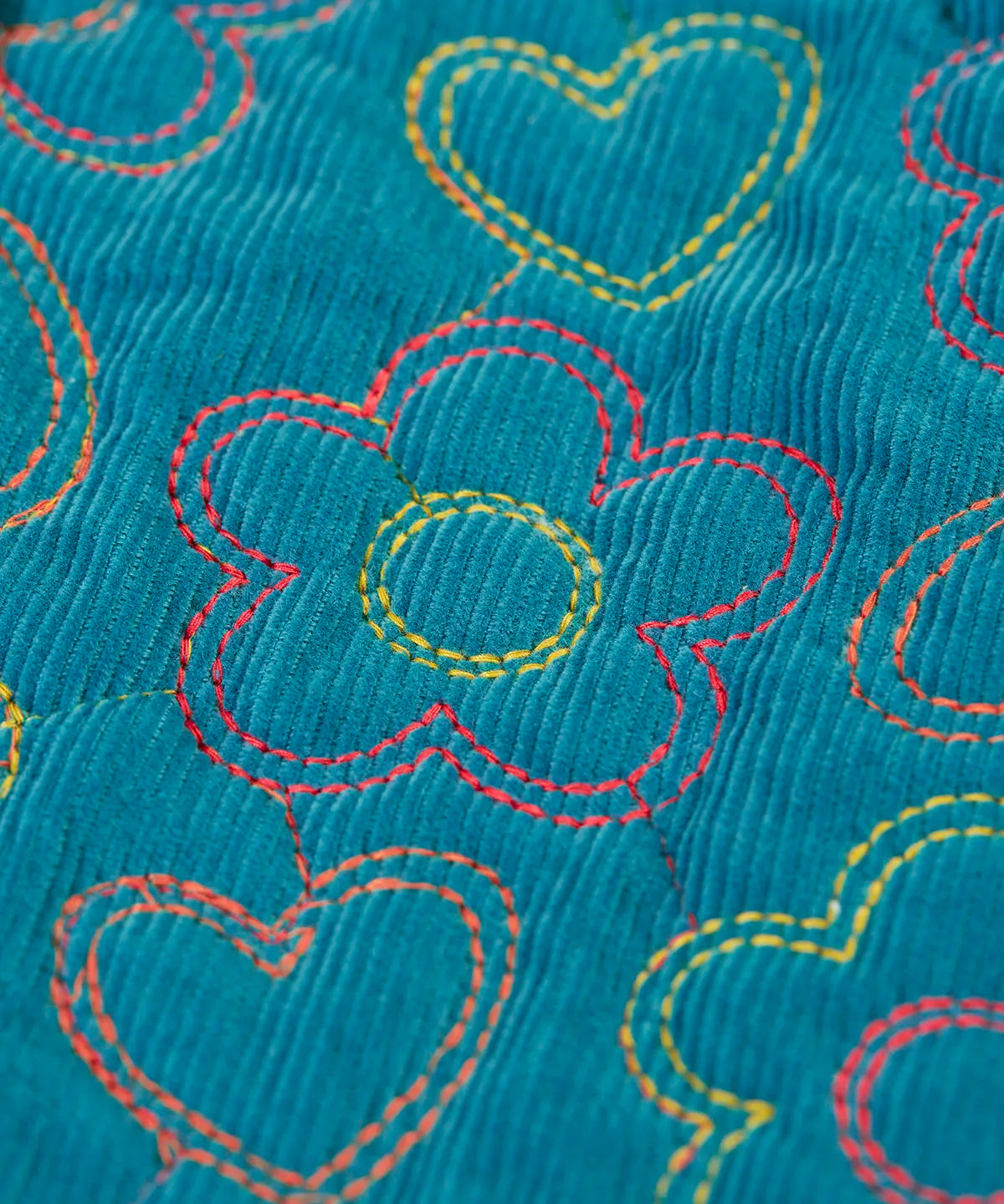 Close up of the floral embroidery on the Frugi Katie quilted cord jacket in boat blue. Flowers and hearts in various colours.