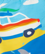 Close up of the camper van on the Frugi blue skies beach kids board shorts. A white camper with red, orange and yellow stripe on the body and a green surf board on it's roof