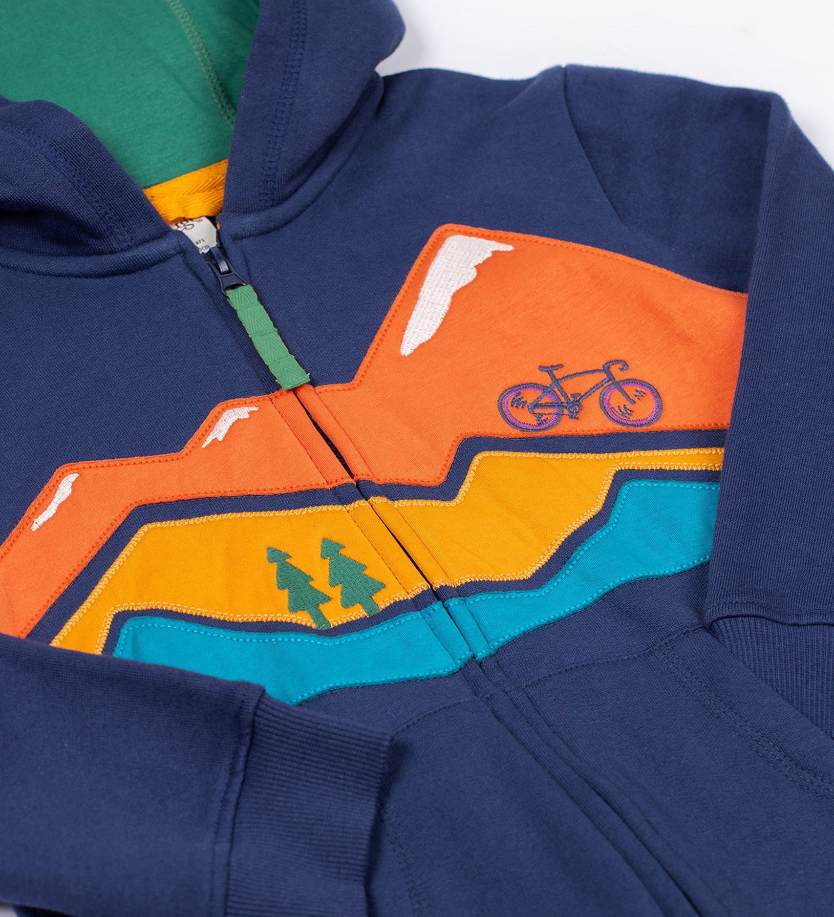 A close up of the Frugi kids carbis hoodie in navy/blue mountain showing the mountainscape applique detail over the full length zip