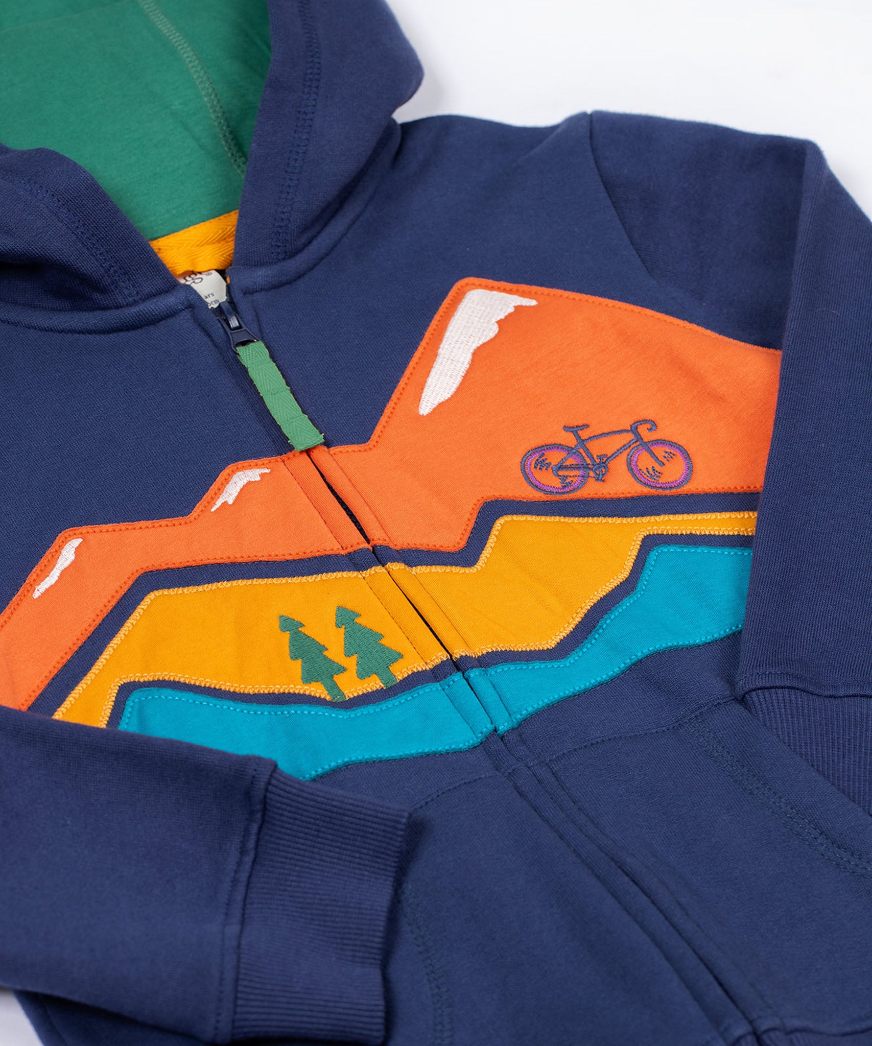 A close up of the Frugi kids carbis hoodie in navy/blue mountain showing the mountainscape applique detail over the full length zip