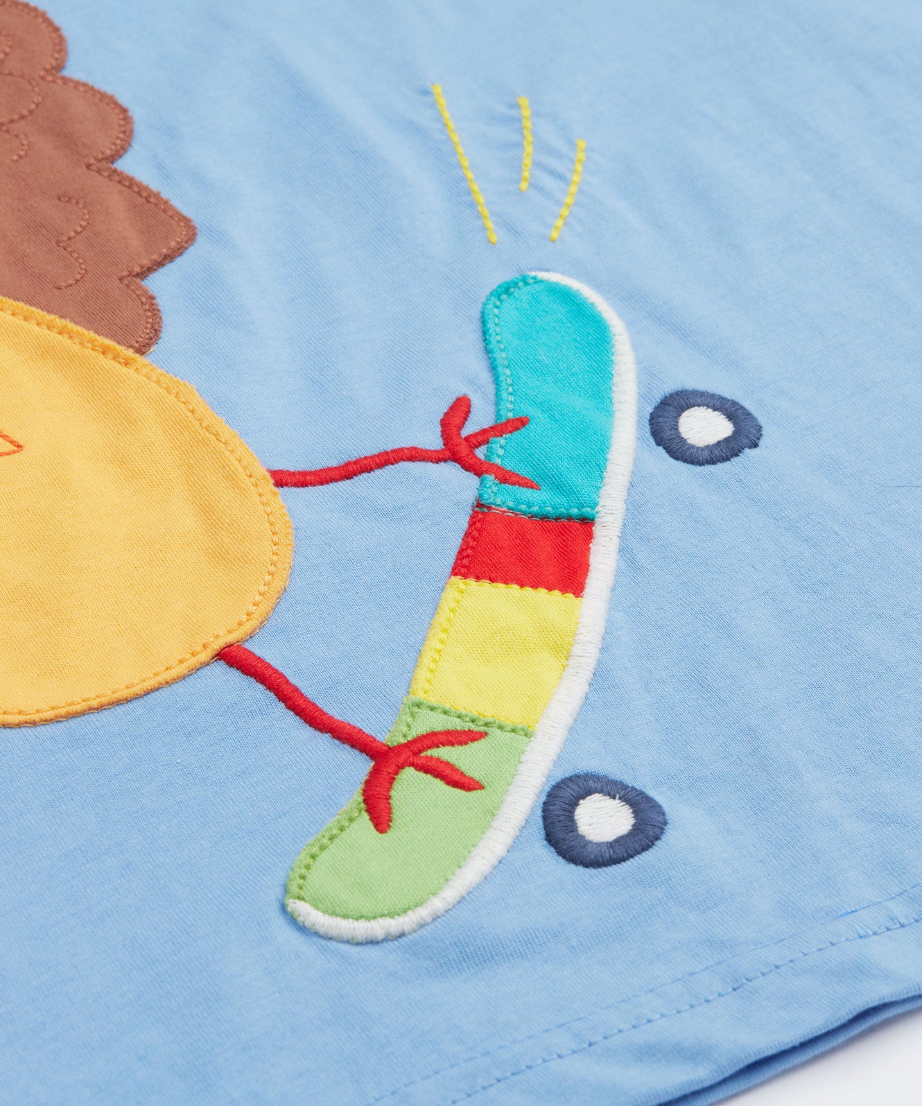 Close up of the Frugi kids cornflower blue chicken t-shirt. Showing the appliqué detail of the skateboard on light blue organic cotton fabric