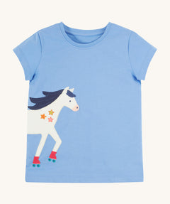 Frugi Elise Wrap Around T-Shirt in cornflower blue – GOTS organic cotton kids' t-shirt with short sleeves, featuring a playful appliqué of a white horse with roller skates that continues from the front to the back.