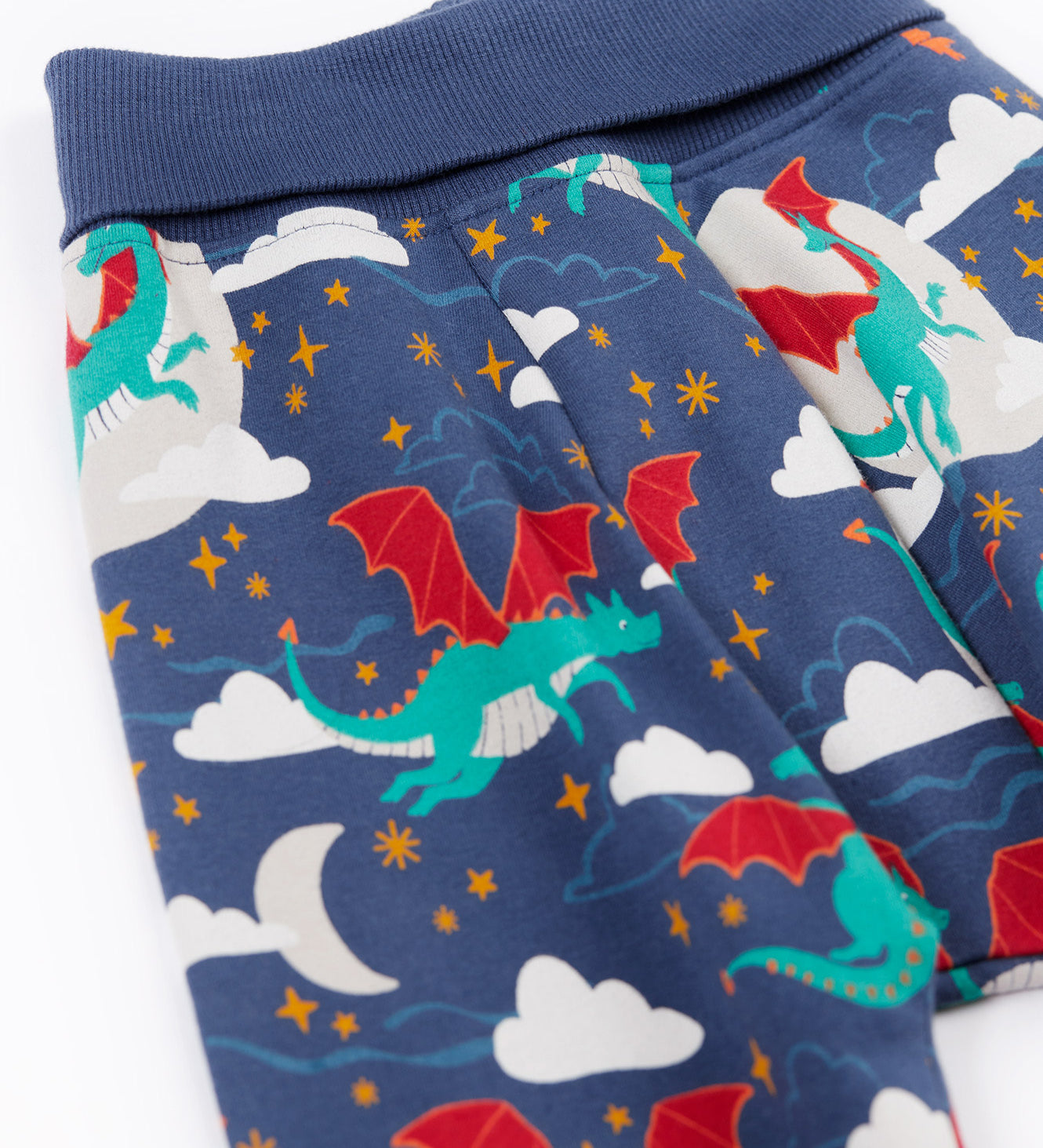 A close up of the fold-able waist band on the Frugi Organic Cotton Cosy Parsnip Pants with a Dragon Skies print. A navy coloured trousers with a print featuring a green coloured dragon. clouds and stars. These trousers are part of a wide range of organic cotton clothing for children available here at Babipur. 