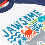A smiling child wearing the Frugi Reid Raglan T-Shirt - Jawsome. A colourful t-shirt made from GOTS Organic cotton  with a white body with sea-life animal print