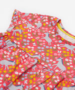 Close up of the Frugi kids Ellen dress donkey drove. Showing the turned up short sleeve and neck detail. Features grey donkeys surrounded by yellow white pink and light blue flowers on a light pink organic cotton fabric 