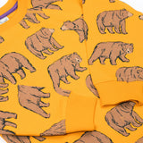 A close up of the Frugi kids Ethan printed sweater in beary wild. Showing the elasticated cuff detail on the arm on dark yellow organic cotton fabric.