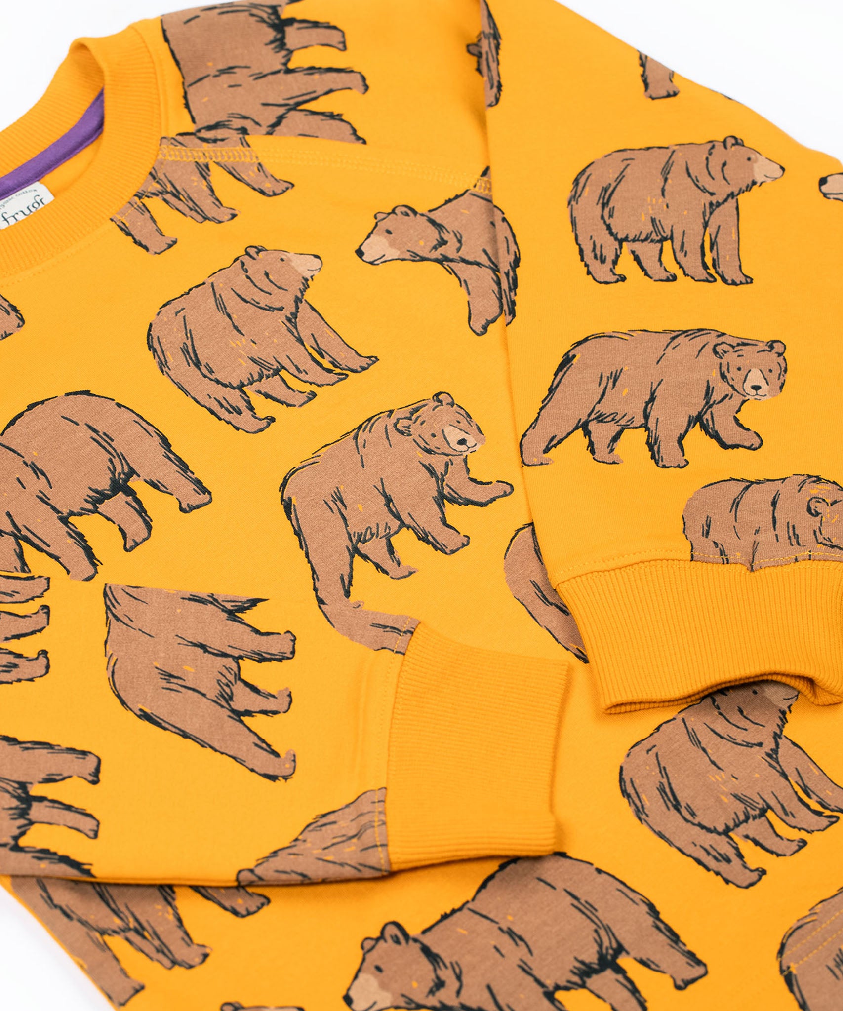 A close up of the Frugi kids Ethan printed sweater in beary wild. Showing the elasticated cuff detail on the arm on dark yellow organic cotton fabric.