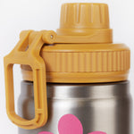 A close up of the Frugi kids Insulated bottle in fun flowers. Showing the yellow cap with loop detail. 