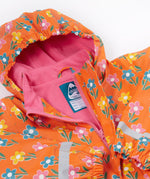 A close up of the Frugi kids fun flowers puddle buster coat showing the multicolour flowers on orange waterproof material. Features a full length zip and velcro fasteners for a secure fit.