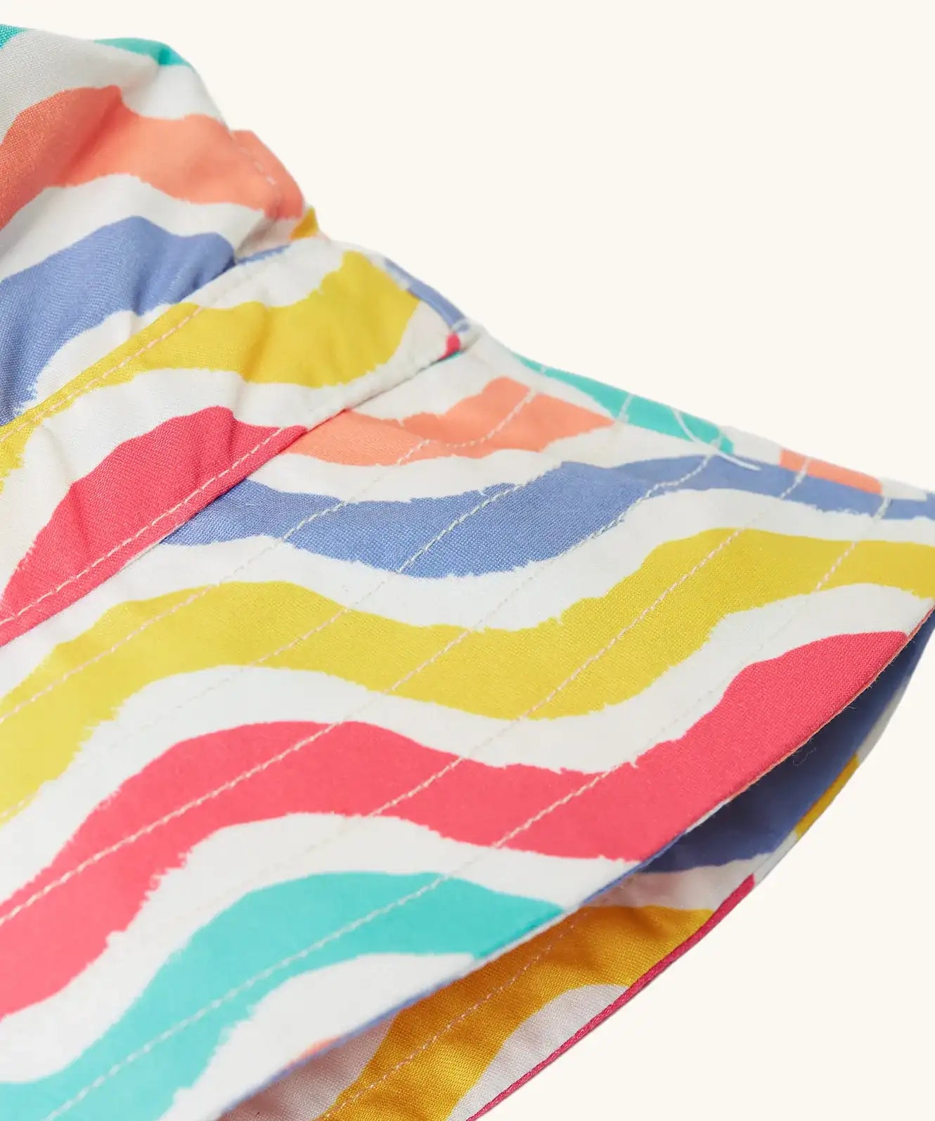 Close up of the brim on Frugi adjustable swim hat with a rainbow wave print in pink, white, yellow, purple, peach and turquoise.