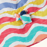 Close up of the toggle on the Frugi adjustable swim hat with a rainbow wave print in pink, white, yellow, purple, peach and turquoise.