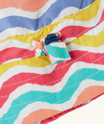 Close up of the toggle on the Frugi adjustable swim hat with a rainbow wave print in pink, white, yellow, purple, peach and turquoise.