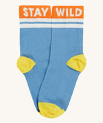 Close up of the Frugi light blue sunnie socks. Showing the 'stay wild' slogan on the orange ankle cuff. Features a light yellow heel and toe contrast panel on light blue organic cotton fabric
