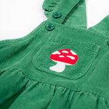 A close up of the frugi kids isla dugaree dress in holly green/mushroom showing the mushroom embroidery detail on the small front pocket and corduroy detail on green organic cotton fabric.