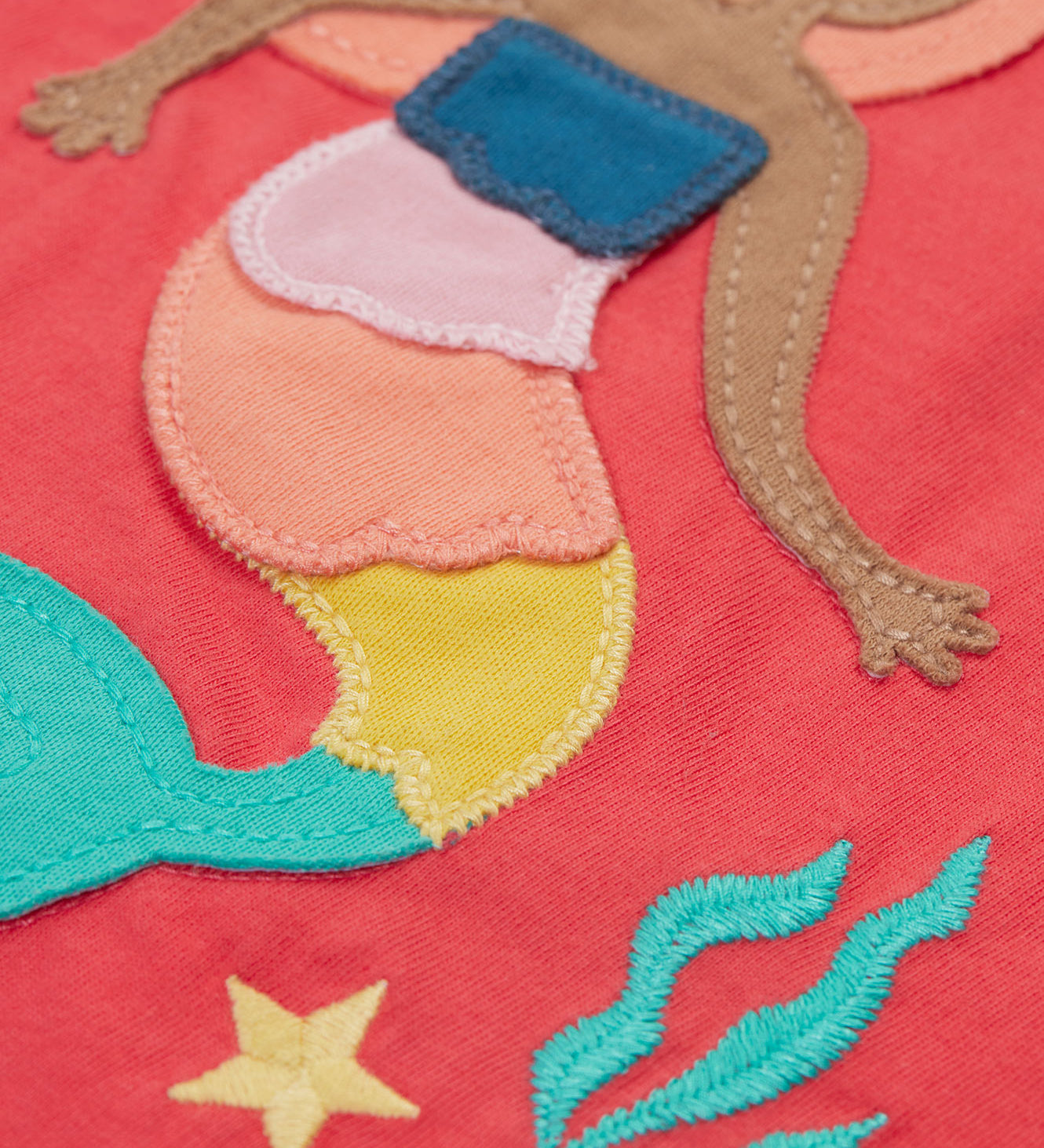 A close up of the Frugi Tamara t-shirt showing the mermaid appliqué on the  front next to the embroidered coral and star on light pink organic cotton fabric