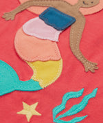 A close up of the Frugi Tamara t-shirt showing the mermaid appliqué on the  front next to the embroidered coral and star on light pink organic cotton fabric