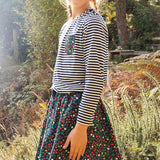 Girl stood in the woods wearing a striped top and the Frugi floral print maeve twill skirt