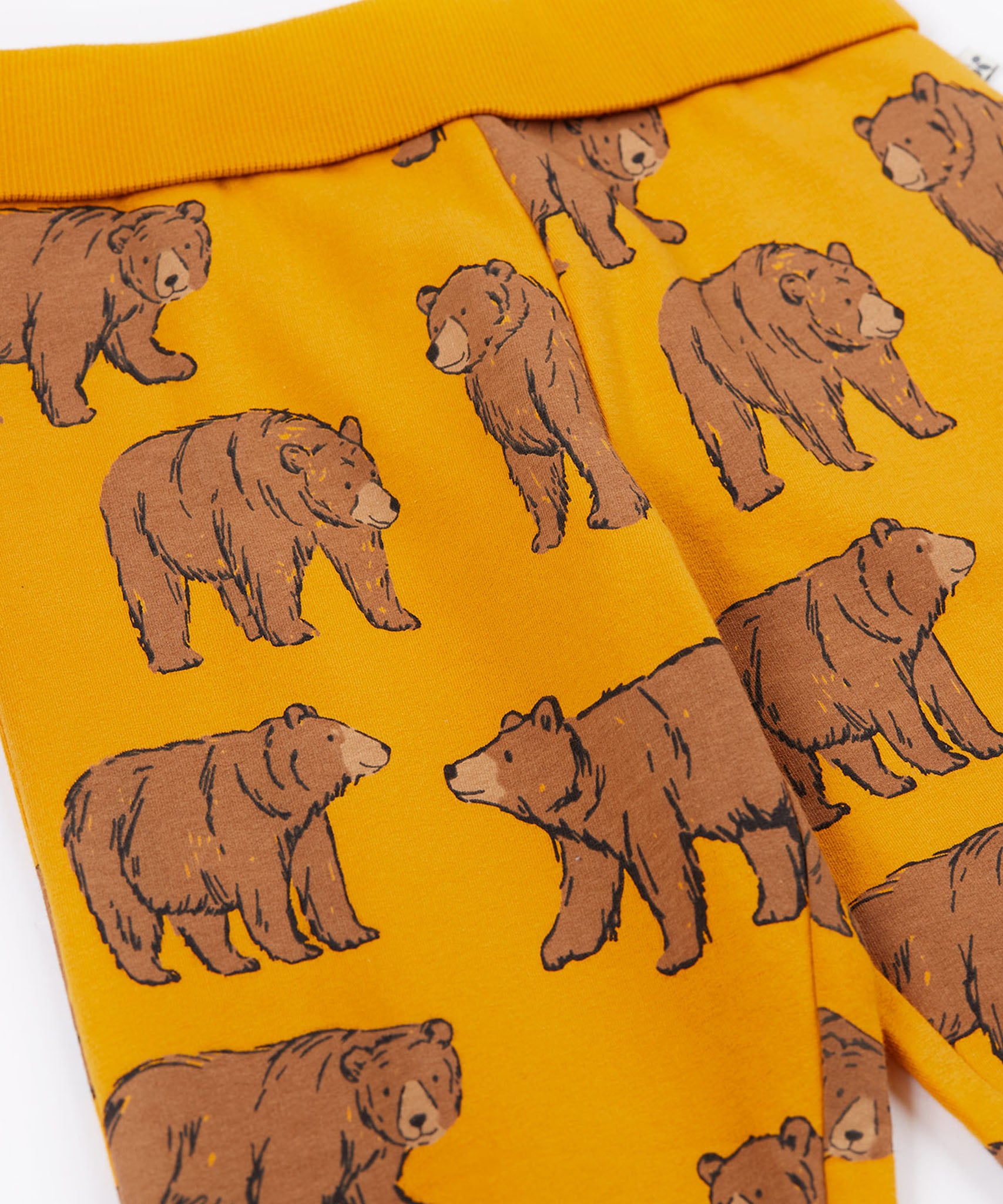 A close up of the Frugi kids beary wild parsnip joggers showing the bear print detail and turn up waist hem on dark yellow organic cotton fabric.