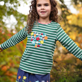A little girl in the forest wearing an organic cotton Frugi outfit - the Cara Corduroy Skirt with flower embroidery, and a long sleeved embroidered stripy top.