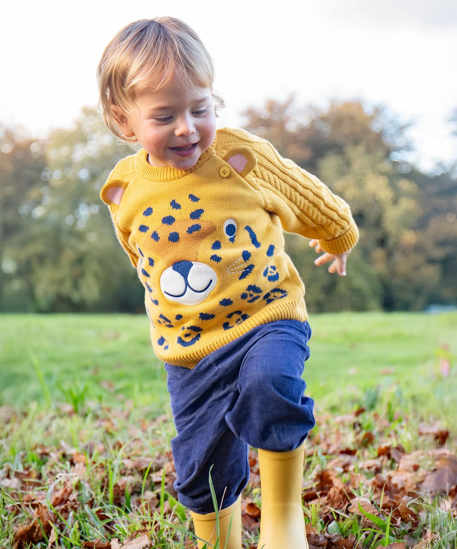 A little toddler boy wearing the Frugi organic cotton leopard knitted jumper and the Frugi organic cotton cord pull ups in Ink Blue.