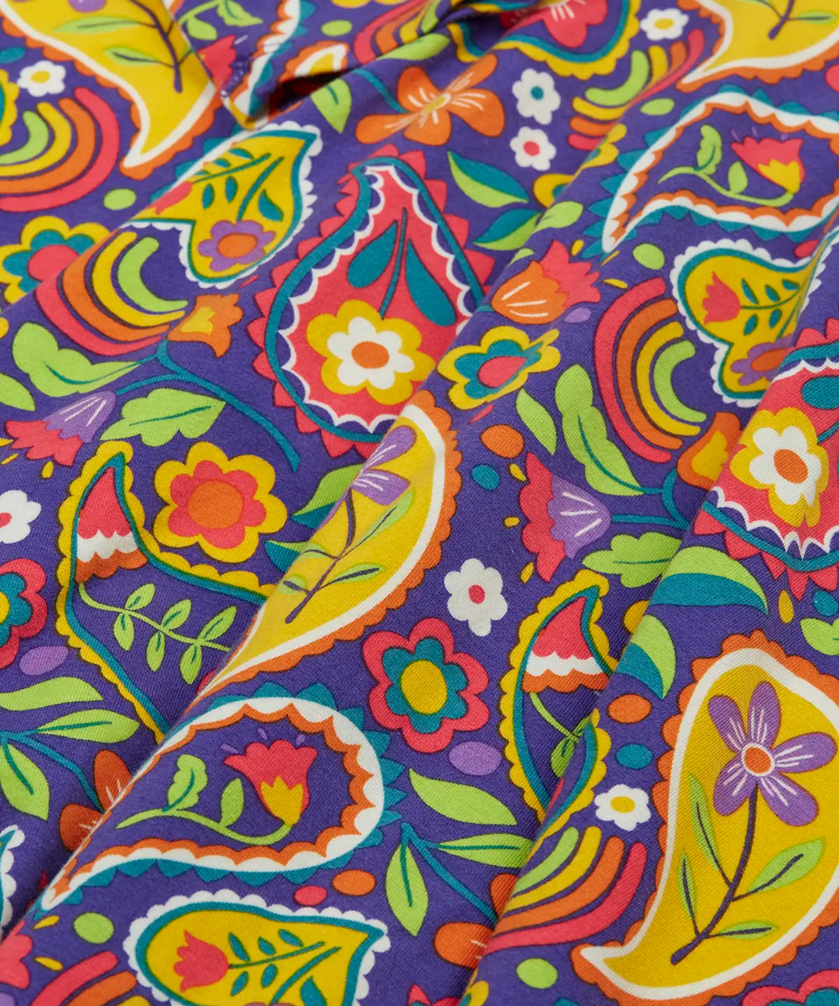 Close up of the folds on the skirt on the Frugi GOTS organic cotton sofia skater dress in pretty paisley. Purple background with colourful paisley print featuring flower and rainbow details.