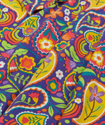 Close up of the folds on the skirt on the Frugi GOTS organic cotton sofia skater dress in pretty paisley. Purple background with colourful paisley print featuring flower and rainbow details.