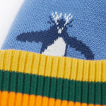 A close up of the Frugi reversible voyager hat showing the penguins design on blue GOTS organic cotton fabric with a yellow, green and orange soft ribbed trim