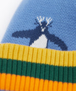 A close up of the Frugi reversible voyager hat showing the penguins design on blue GOTS organic cotton fabric with a yellow, green and orange soft ribbed trim
