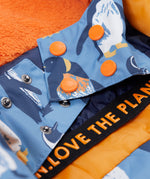 A close up of the Frugi kids snow and ski coat in penguin waddle showing the snow skirt detail in matching penguin waddle print and orange popper fasteners